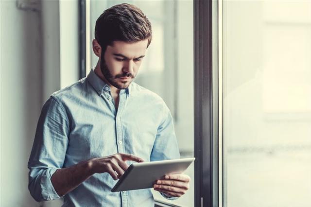 Man standing near window using a tablet with his finger