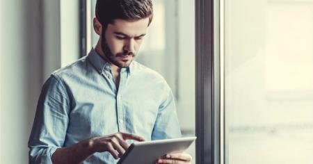 Man standing near window using a tablet with his finger